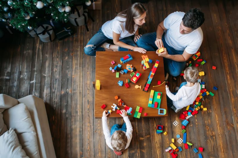 Ariel shot of two children and their parents playing with Lego on a wooden table.