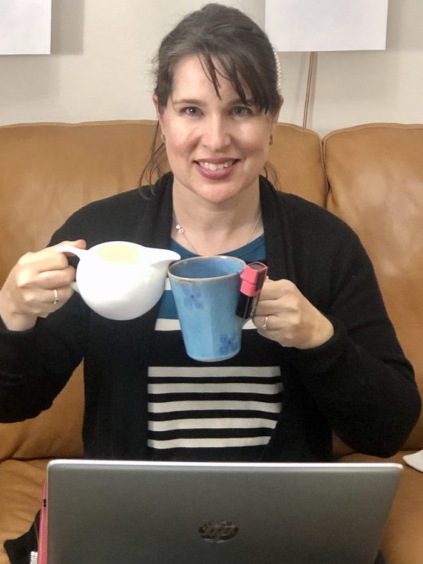 Rebecca sits in front of a laptop with a jar in one hand and cup of coffee in the other with spill device attached to it