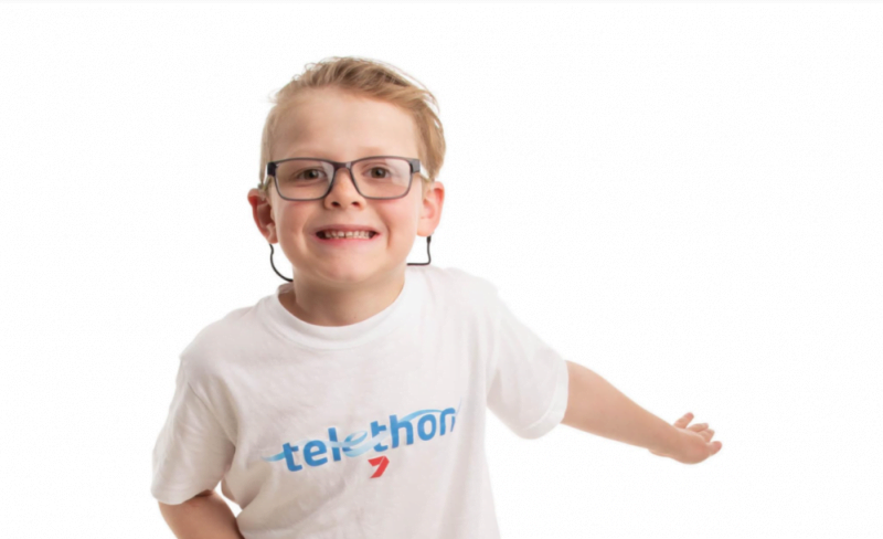 Eamon in a Telethon shirt with his arms stretched out. He's smiling and wearing glasses.