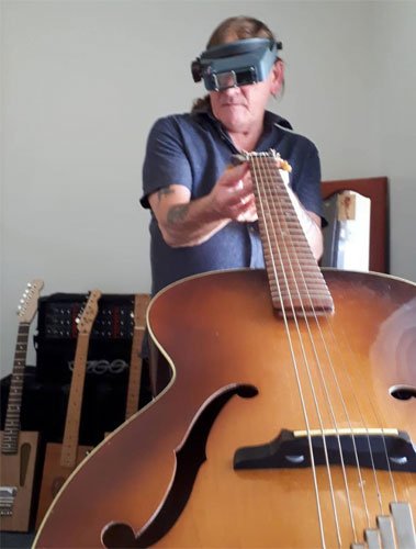 Les, wearing magnifying glasses, looks over a guitar