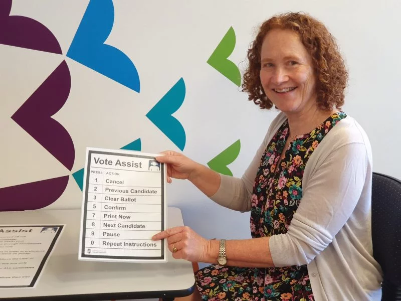 Braille Officer Leone Carrol holds up a Vote Assist poster