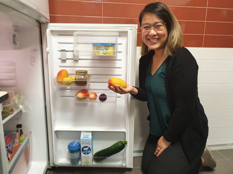 Rachel kneels next to her fridge holding a mango