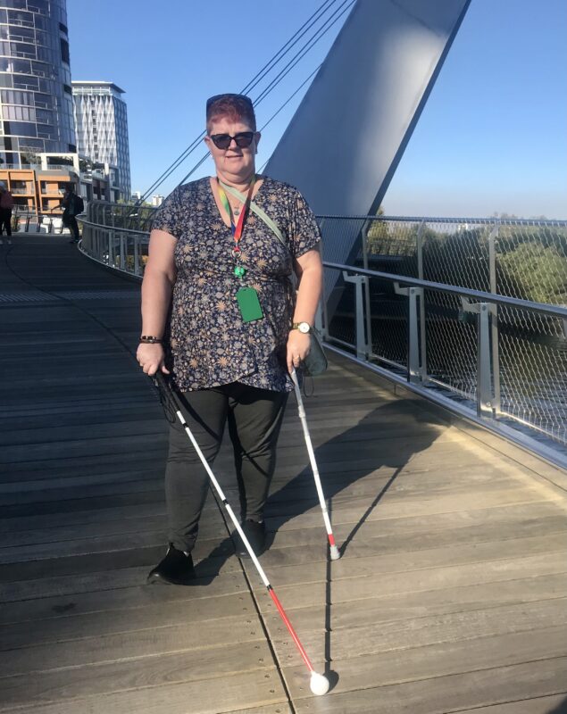 Joanne stands on a bridge holding two canes in her hands