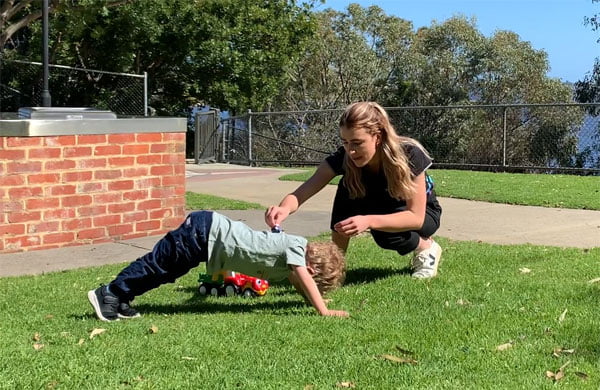 Max forms a bridge while Physiotherapist, Emma drives a toy car over Max's back