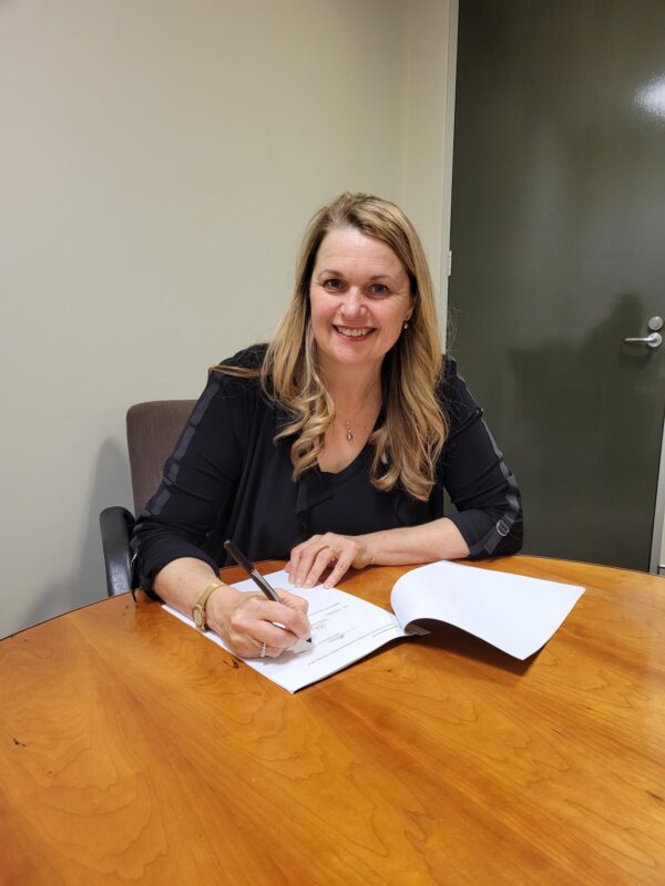 Our CEO signs the State Library partnership. She's seated around a round wooden table.