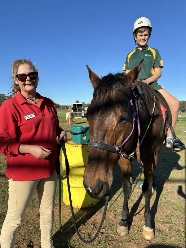 Veronica holds the lead while standing beside a horse with a child sitting on it.