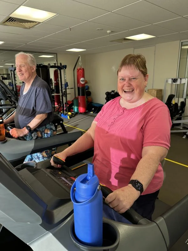 Jenny smiling and walking on the treadmill beside her husband Trevor.