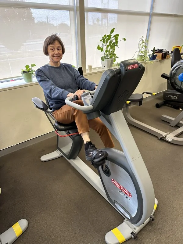 Lindy riding an exercise bike in the VisAbility Gym. 